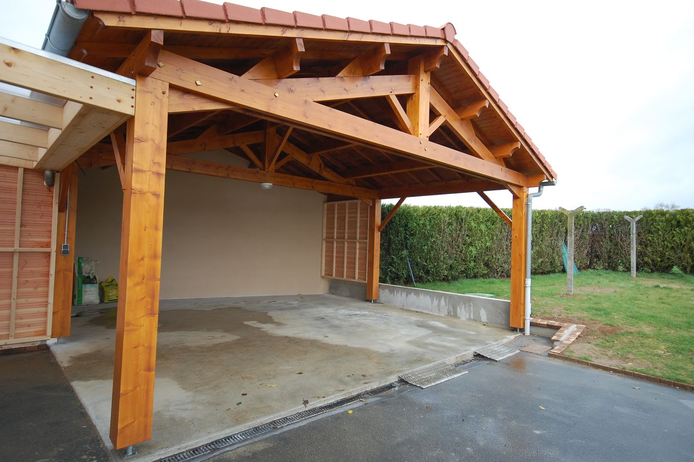 Car-port en charpente bois apparente, ferme et arbalétriers visibles sous la couverture