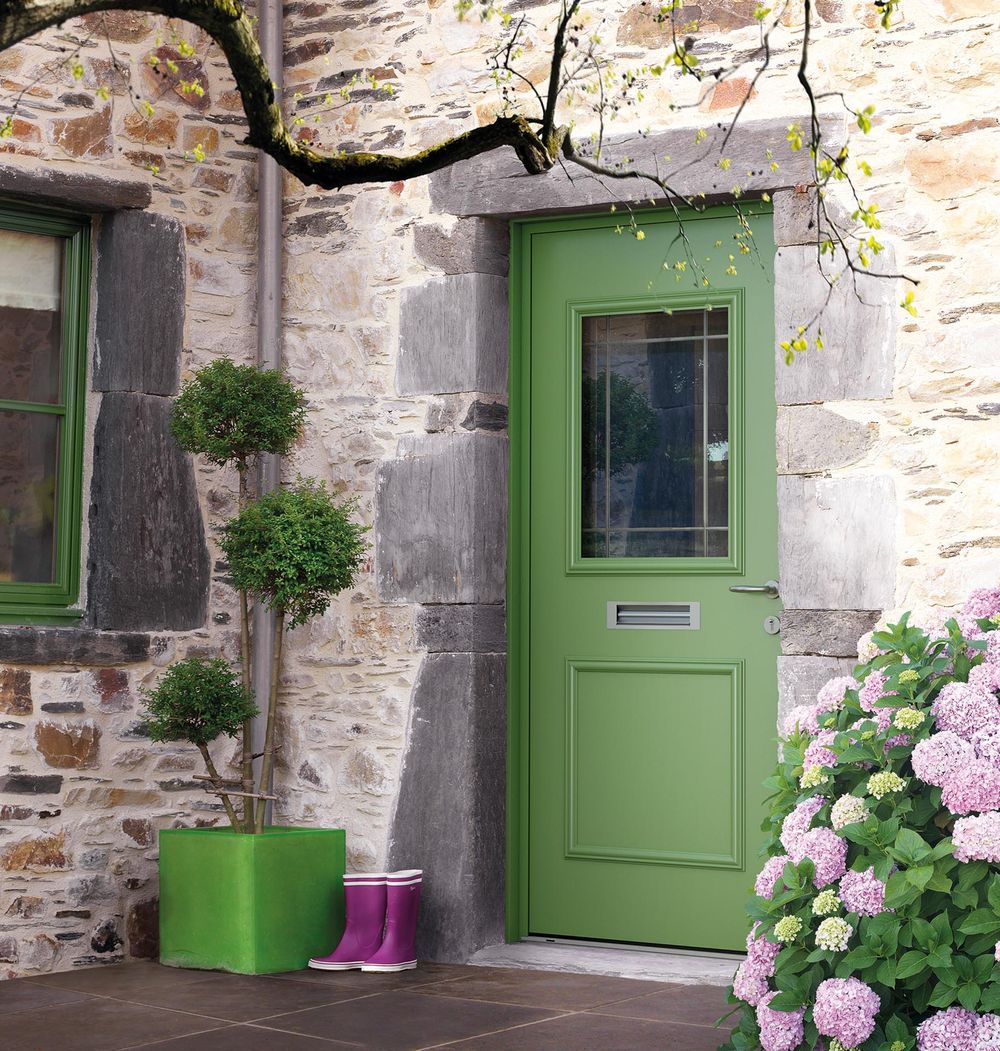 Porte d'entrée verte posée dans un mur de pierre, entourée d'hortensias