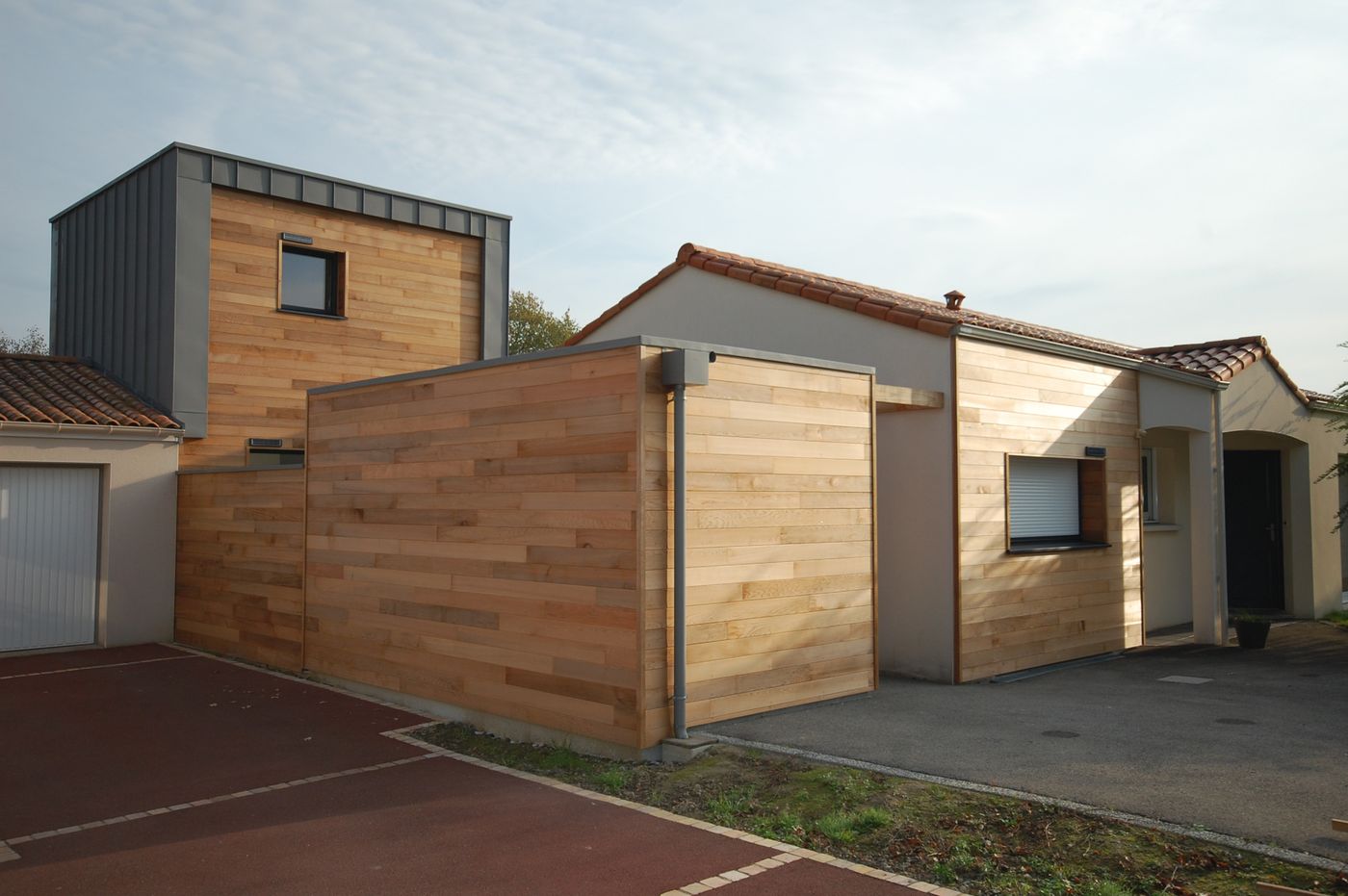 Extension de plain-pied habillée d'un bardage bois clair devant une maison ancienne